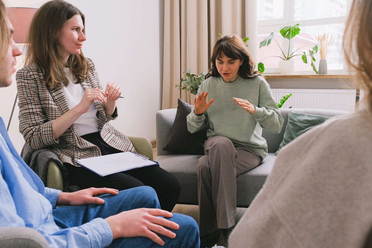A woman expresses herself passionately in a group therapy session while the therapist and others listen attentively.