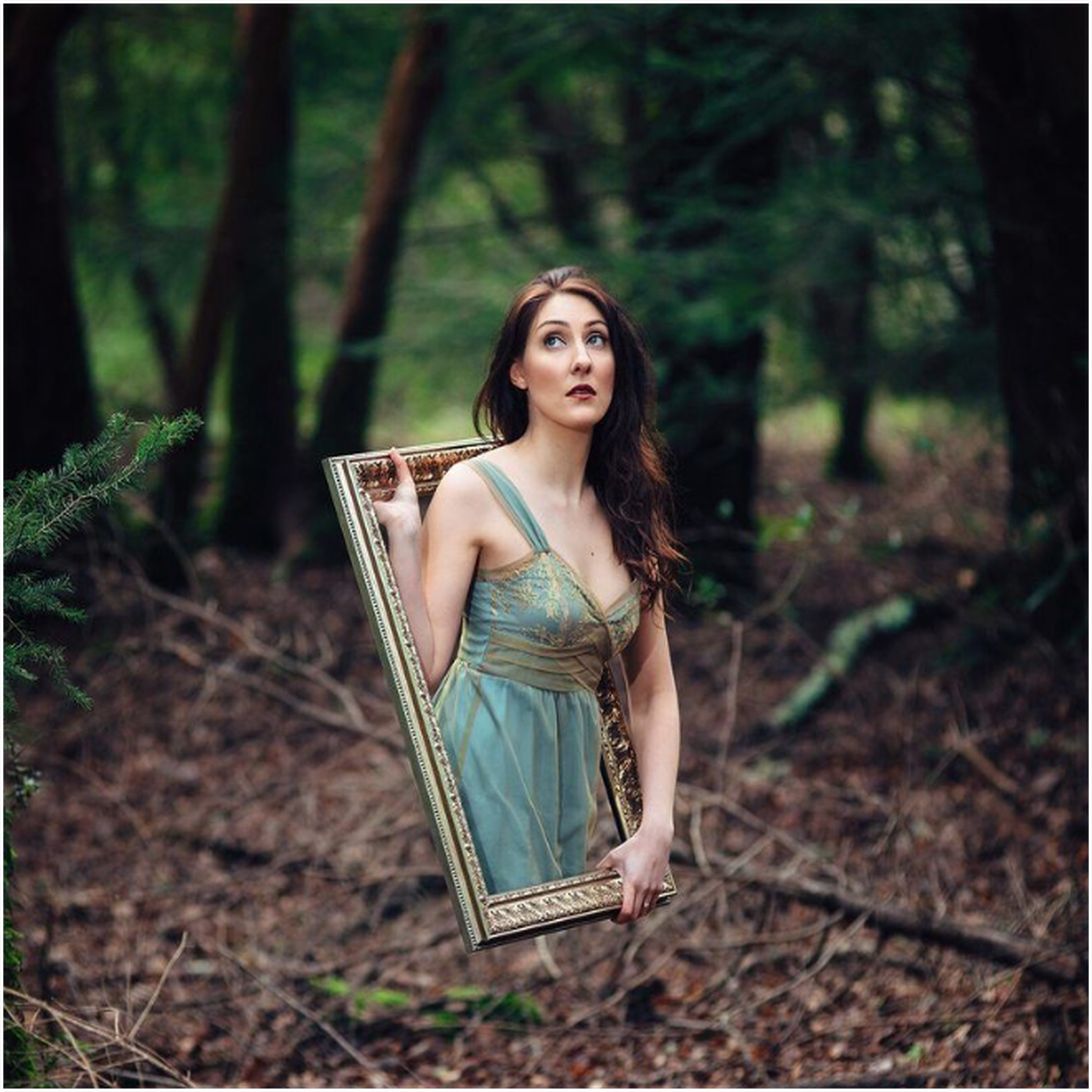 A woman appears to emerge from a mirror frame held in front of her in a forest, creating a magical illusion. A woman appears to emerge from a mirror frame held in front of her in a forest, creating a magical illusion.