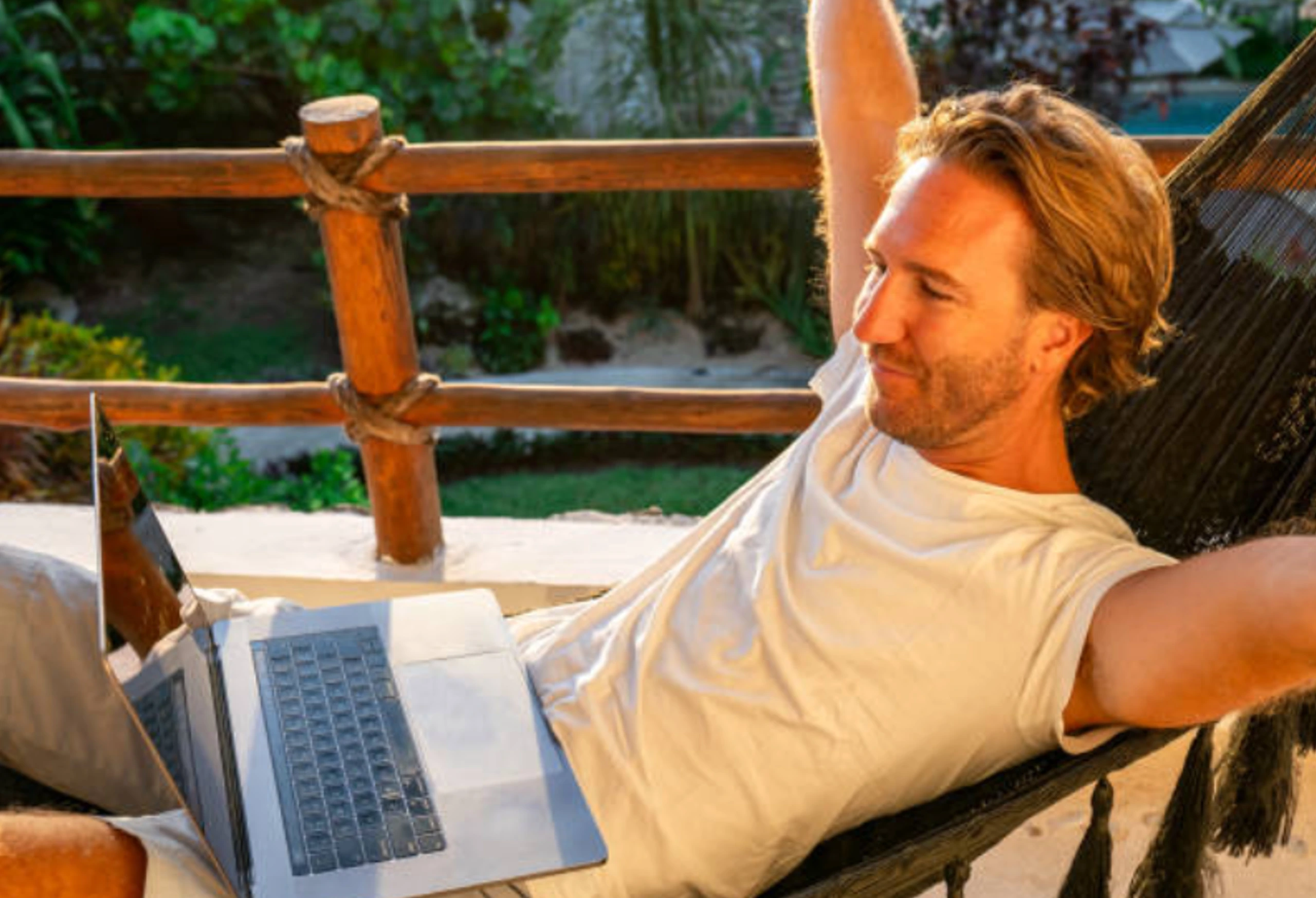 A relaxed man working on a laptop while lounging in a hammock outdoors.